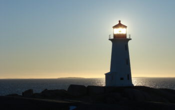 Pegg's Cove lighthouse backlit by the sun at dusk.