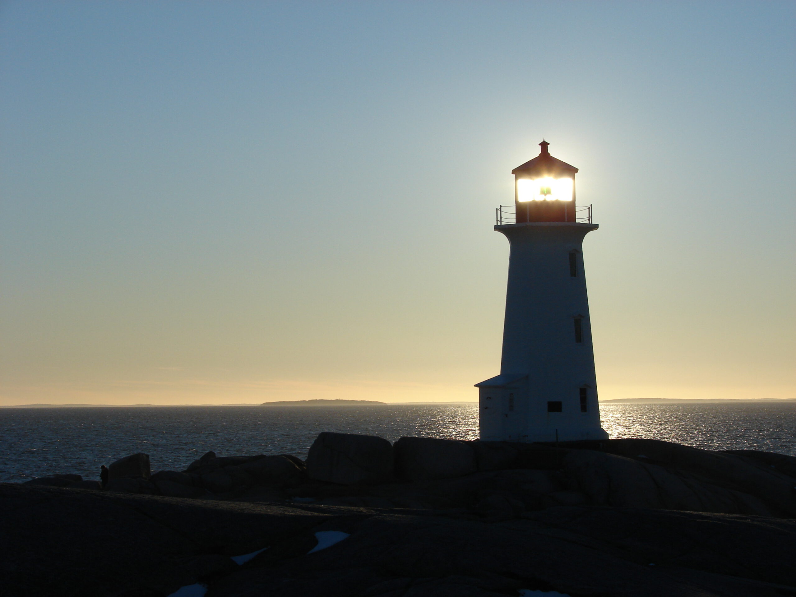 Pegg's Cove lighthouse backlit by the sun at dusk.