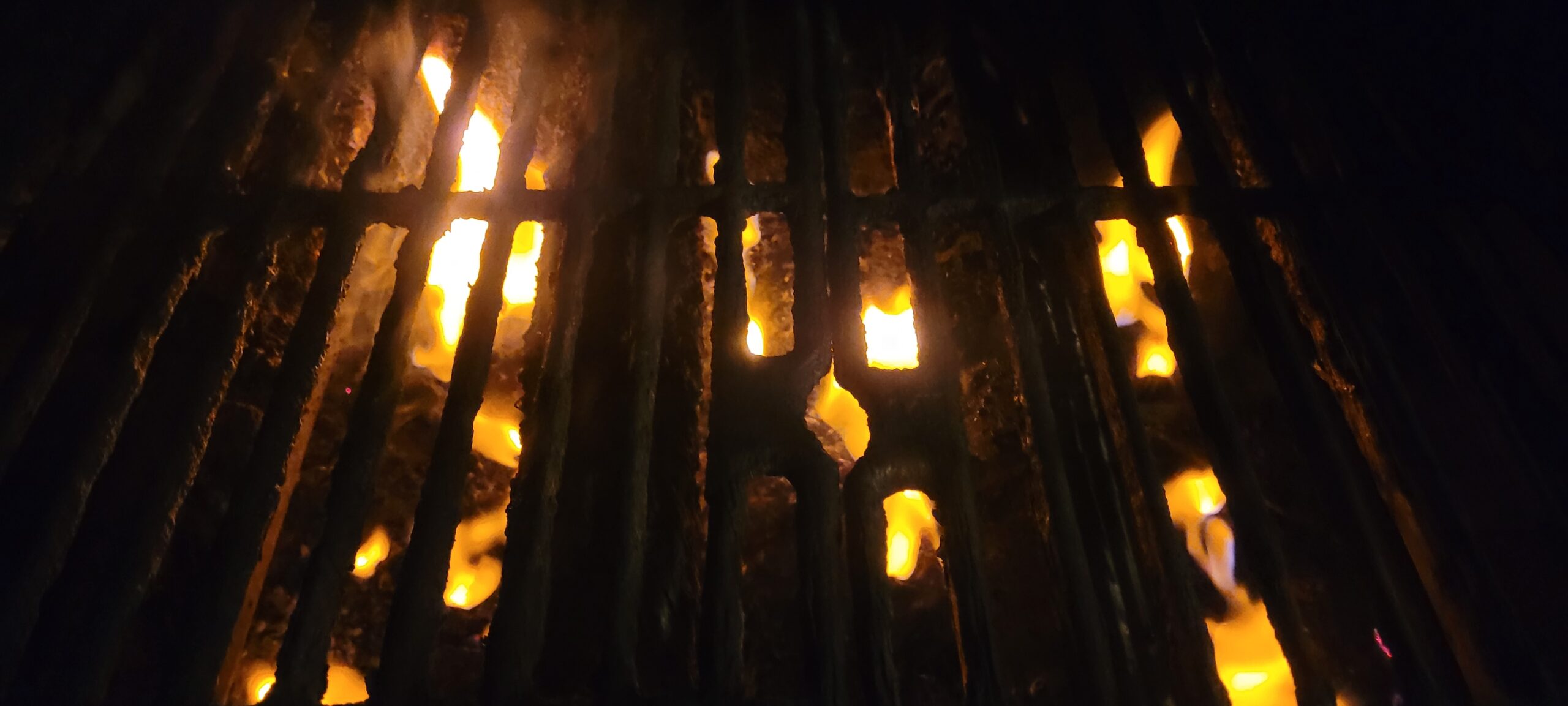 Flames burning behind an old, worn, iron grill.